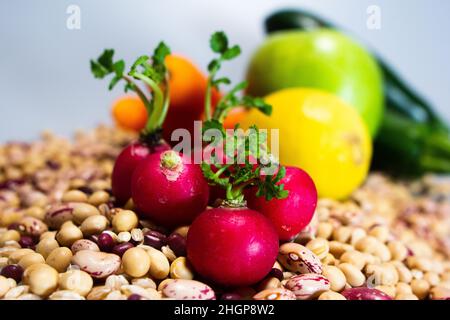 Veganes Essen: Rote Radieschen auf Pinto-Bohnen, Perlgerste, Soja, Azuki-Bohnen mit Zitrone, Zucchini, Karotten und Apfel auf dem Boden Stockfoto