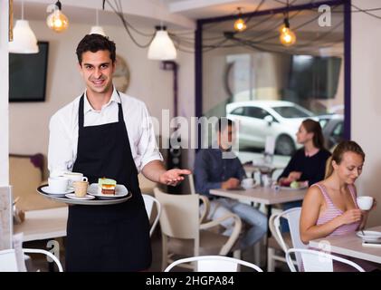 Porträt eines jungen Kellners, der zum Kaffee einlädt Stockfoto