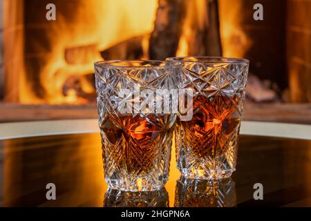 Zwei Gläser Whisky mit Eis auf einem Hintergrund eines brennenden Kamins. Stockfoto