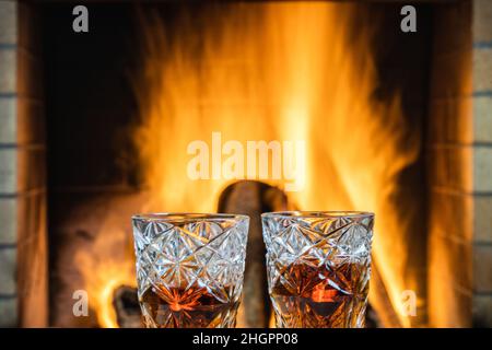 Zwei Gläser Whisky mit Eis auf einem Hintergrund eines brennenden Kamins. Stockfoto