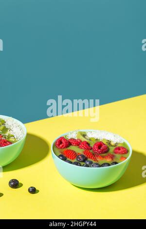 Smoothie Schüssel mit frischen Beeren und Früchten in blauer Platte auf gelb dunklen Schatten Stockfoto