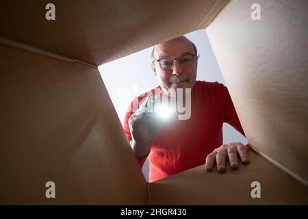 Senior überraschte den Mann in Gläsern, die auspacken, den Karton öffnen und nach innen schauen. Das Paket, Lieferung, Überraschung, Geschenk Lifestyle-Konzept. Stockfoto