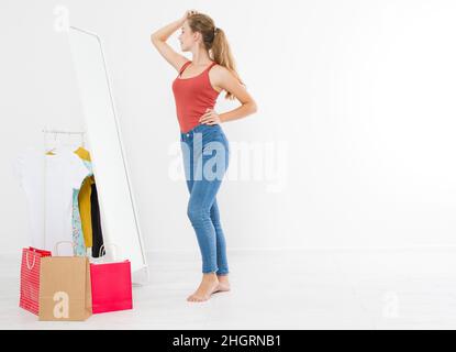 Shopping-Verkaufskonzept. Blonde Mädchen in Jeans und T-Shirt. Junge Frau in guter Körperform Blick auf Spiegel und Gewicht zu verlieren. Speicherplatz kopieren Stockfoto