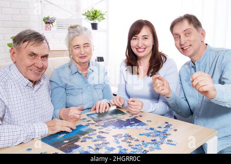 Glückliche ältere Eltern und ein Paar mittleren Alters, die zu Hause an einem Puzzle arbeiten Stockfoto