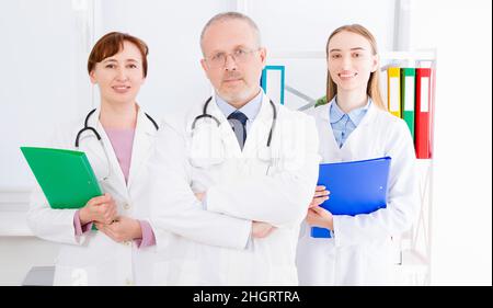 Arzt, der im Büro mit medizinischem Personal posiert, trägt ein Stethoskop. Hochwertiges Medizinkonzept. Mann in weißer Uniform. Krankenversicherung. Selektiv Stockfoto