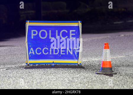 Ein Polizeischild und ein Kegel, die eine Straße blockieren und herannahende Autofahrer vor einem Unfall in der Nähe warnen. Stockfoto