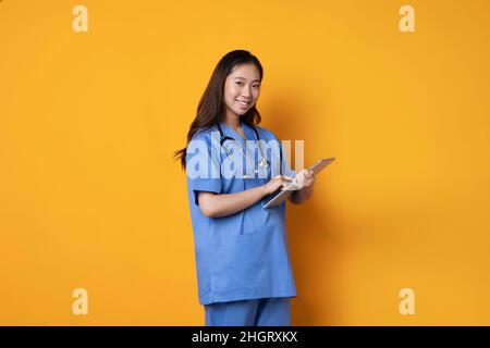 Studiofoto mit orangefarbenem Hintergrund einer Ärztin, die lächelnd auf einen Ordner zeigt Stockfoto