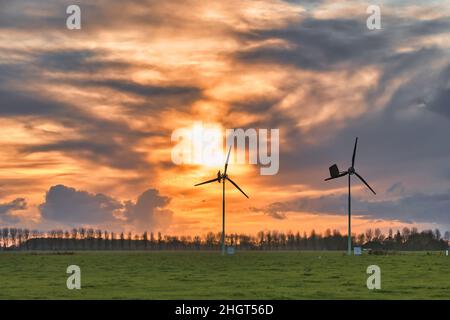 Zwei Windturbinen auf einer Weide, in der flachen landwirtschaftlichen niederländischen Provinz Groningen, wurden bei Sonnenuntergang vor einem dramatischen Himmel geschildet. Stockfoto