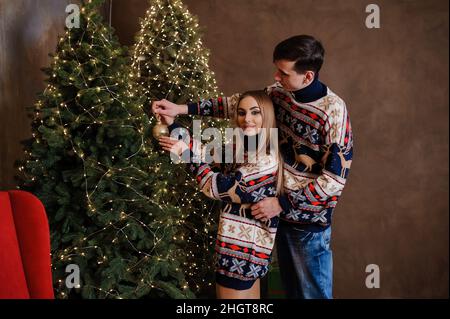 Ein Mann und ein Mädchen umarmen und küssen sich vor dem Hintergrund eines Weihnachtsbaums und eines roten Sofas Stockfoto