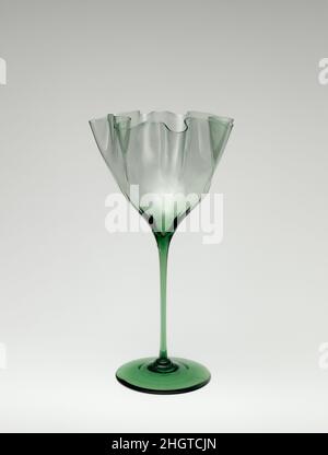 Vase mit hohen Stielstämmen ca. 1890 Harry Powell British zugeschrieben Dieses Objekt ist ein sehr schönes Beispiel für die Vasen-Serie, die von Harry Powell entworfen wurde (Enkel des Weinhändlers James Powell, der 1834 die Whitefriars Glassworks gekauft hatte). Harry Powells Entwürfe der 1880s und ‘90s schufen eine ganze Gruppe von dekorativen Gefäßen, die sich durch zart unregelmäßige, gewellte Schalen und dezent getöntes Glas auszeichneten. Die Feinheit des Glases, verstärkt durch die Rüschen der Schale, ist vom venezianischen cristallo inspiriert. Das flüssige Design der zart unregelmäßigen Schale, scheinbar organisch aus n geboren Stockfoto