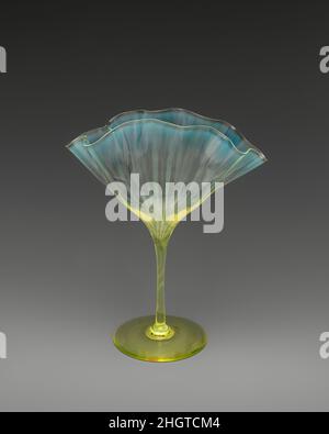 Fächerförmige Vase ca. 1890 Harry Powell British zugeschrieben Dieses Objekt ist ein sehr schönes Beispiel für die Vasen-Serie, die von Harry Powell entworfen wurde (Enkel des Weinhändlers James Powell, der 1834 die Whitefriars Glassworks gekauft hatte). Harry Powells Entwürfe der 1880s und ‘90s schufen eine ganze Gruppe von dekorativen Gefäßen, die sich durch zart unregelmäßige, gewellte Schalen und dezent getöntes Glas auszeichneten. Die Feinheit des Glases, verstärkt durch die Rüschen der Schale, ist vom venezianischen cristallo inspiriert. Das flüssige Design der zart unregelmäßigen, fächerförmigen Schale zeugt von der sk Stockfoto