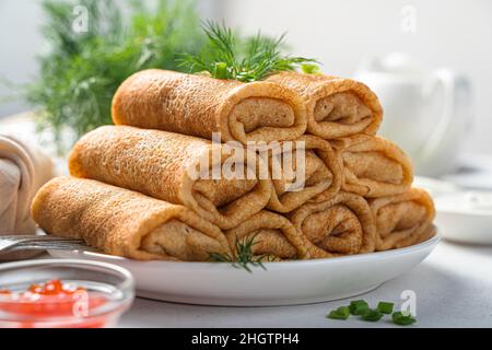 Ein Stapel Pfannkuchen mit Fleisch auf einem weißen Teller, der mit frischem Dill dekoriert ist. Seitenansicht Nahaufnahme. Traditionelle Pfannkuchen für Maslenitsa. Stockfoto