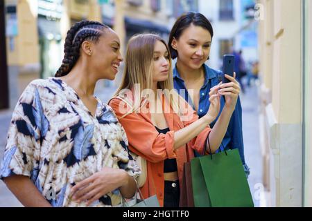 Modische multirassische Damen, die beim Einkaufen in der Stadt Fotos auf dem Smartphone machen Stockfoto