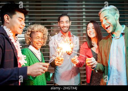 Multiethnische, tausendjährige Gruppe von Freunden, die Wunderkerzen zusammenfalten. Stockfoto