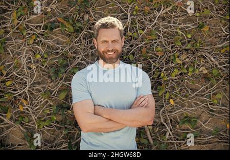 Happy bärtig reifen Mann im Sommer Shirt auf Pflanzen Wand Hintergrund, Sommer-Stil Stockfoto