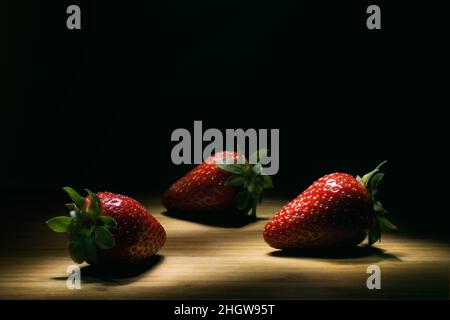 Drei Erdbeeren auf einem Holzboden mit hohem Kontrast. Stockfoto