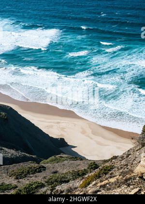 Türkisfarbene Wellen schlagen am Strand Praia do Castelejo in der Algarve in Portugal Stockfoto