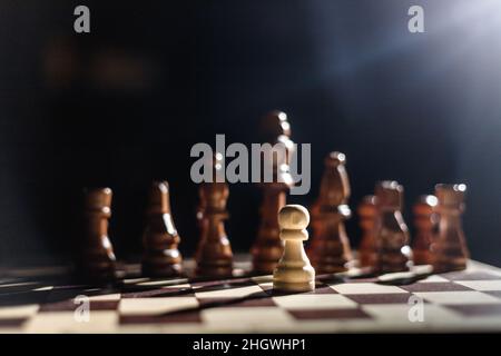 Eine Spielfigur, die sich gegen eine ganze Reihe schwarzer Schachfiguren aufsetzt. Einer gegen alle. Held Stockfoto