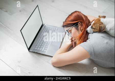 Der Student schlief auf dem Boden ein, während er hart studierte. Vorbereitung auf die Untersuchung während der Sitzung. Freiberuflerin schläft mit ihr an einem Laptop Stockfoto
