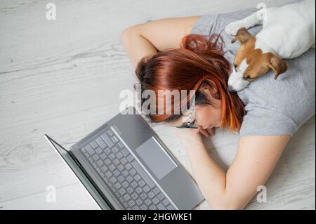 Der Student schlief auf dem Boden ein, während er hart studierte. Vorbereitung auf die Untersuchung während der Sitzung. Freiberuflerin schläft mit ihr an einem Laptop Stockfoto