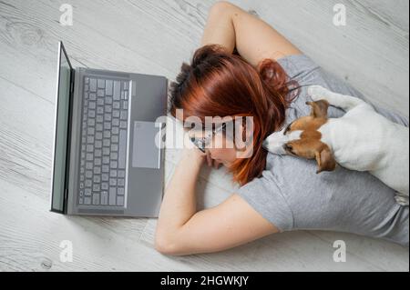 Der Student schlief auf dem Boden ein, während er hart studierte. Vorbereitung auf die Untersuchung während der Sitzung. Freiberuflerin schläft mit ihr an einem Laptop Stockfoto
