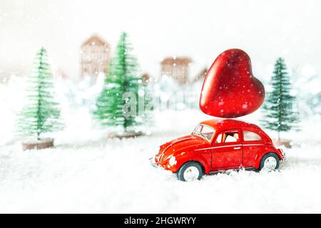 Rotes Retro-Auto mit Herz in einer Winterlandschaft. Postkarte zum Valentinstag. Urlaubslieferung. Selektiver Fokus. Stockfoto