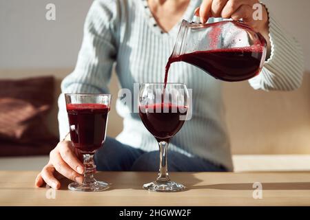 Frau gießt frischen roten Rübensaft aus einem Krug in zwei Gläser in einer sonnigen Wohnung Stockfoto