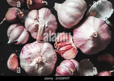 Knoblauchzwiebeln und Knoblauchzehen auf schwarzem Hintergrund. Nahaufnahme, flach liegend, Draufsicht. Lebensmittelhintergrund, selektiver Fokus. Stockfoto