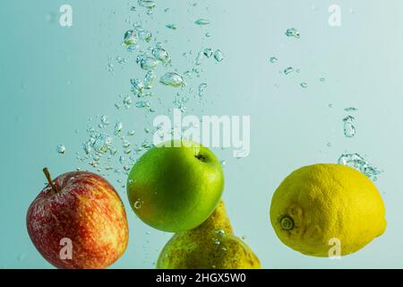 Nahaufnahme von roten und grünen Äpfeln, limon und Birne, die im Wasser fallen. Wunderschöne Hintergründe. Stockfoto