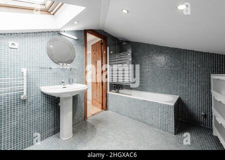 Große Toilette mit schrägen Decken gefliest mit Mosaikfliesen an den Wänden und am Boden mit weißen Toiletten Stockfoto