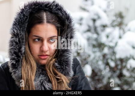 Hübsches Mädchen mit langen Haaren in einem Pelzmantel im Winter unter fallendem Schnee stehen Stockfoto