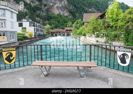 Eine hölzerne Parkbank in der Mitte der beiden Städte Unterseen und Interlaken am Fluss mit türkisfarbener Farbe Stockfoto