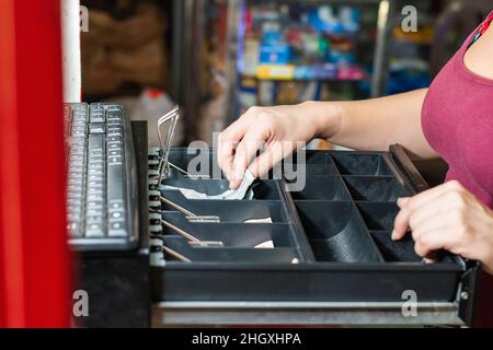 Hand einer unternehmungslustigen Latina Frau in ihrem Geschäft Eröffnung der Kasse. Mädchen vor der Kasse, die Geld nach einem Verkauf. c Stockfoto