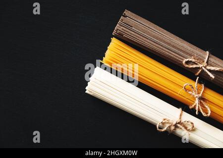 Nudeln aus verschiedenen Ländern. Soba, udon, Spaghetti. Schwarzer Hintergrund, flaches Lay, Kopierbereich. Hintergrund der Speisen. Stockfoto