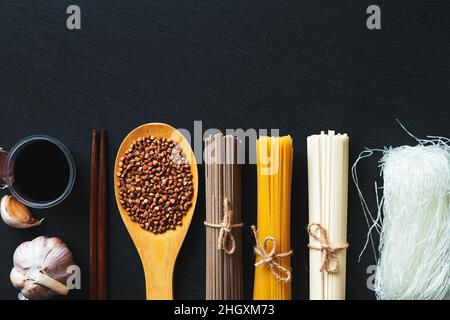 Nudeln aus verschiedenen Ländern. Soba, udon, Spaghetti, funchose. Schwarzer Hintergrund, flaches Lay, Kopierbereich. Hintergrund der Speisen. Stockfoto