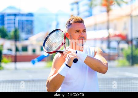 Älterer kaukasischer Mann, der auf dem Tennisplatz Tennis spielt und tagsüber im Freien an der frischen Luft Tennisschläger hält Stockfoto