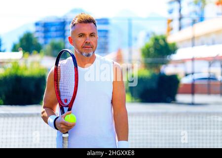 Ein älterer Tennisspieler, der an einem sonnigen Tag im Freien Tennis spielt Stockfoto