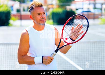 Älterer kaukasischer Mann, der auf dem Tennisplatz Tennis spielt und tagsüber im Freien an der frischen Luft Tennisschläger hält Stockfoto