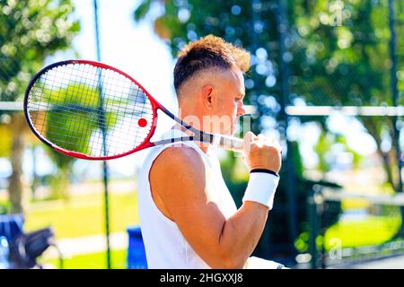 Älterer kaukasischer Mann, der auf dem Tennisplatz Tennis spielt und tagsüber im Freien an der frischen Luft Tennisschläger hält Stockfoto