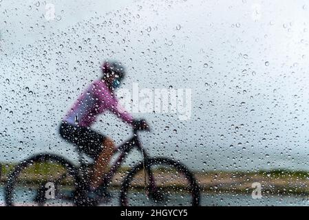 Salvador, Bahia, Brasilien - 15. November 2021: Eine Person, die im Regen mit dem Fahrrad fährt. Salvador, Bahia, Brasilien. Stockfoto