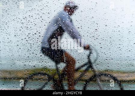 Salvador, Bahia, Brasilien - 15. November 2021: Eine Person, die im Regen mit dem Fahrrad fährt. Salvador, Bahia, Brasilien. Stockfoto