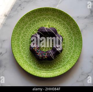 Lila Ube glasiert Mochi Donut mit Streuseln, auf einem grünen Teller mit einem geometrischen Muster. Stockfoto