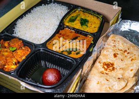 Selektiver Fokus einer Vielzahl von indischen Speisen zum Mitnehmen in einem schwarzen Plastikbehälter. Stockfoto