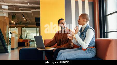 Zwei junge Geschäftsleute, die in einer Bürolobby eine wichtige Diskussion führen. Zwei junge Unternehmer arbeiten in einem Co-Working Spa an einem neuen Projekt zusammen Stockfoto