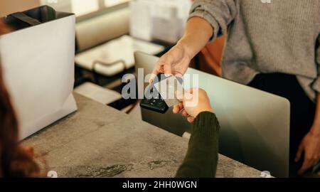 Nicht erkennbarer Kunde, der am Checkout-Schalter mit einer Kreditkarte bezahlt. Die Hand einer Frau klopft auf eine Bankkarte eines kontaktlosen Kreditkartenlesers. Frau Stockfoto