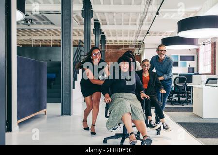 Erfolg mit etwas Spaß feiern. Ein verspieltes Team von Geschäftsleuten, die sich in einem modernen Büro auf Stühlen schieben. Erfolgreiche Geschäftspartner havi Stockfoto