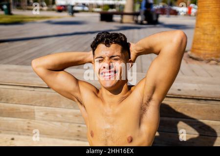 lateinischer Mann, der Sonnencreme auf dem Meer mit Palmen im Hintergrund anwendet Stockfoto