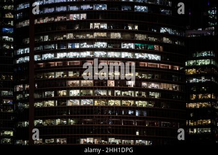 Modernes Bürogebäude mit großen Fenstern in der Nacht Blick aus der Nähe, in den Fenstern leuchtet glühendes Licht und einige Leute im Inneren, Singapur. Stockfoto