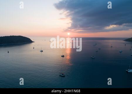 Farbenfroher Sonnenuntergang über der Meeresoberfläche mit Segelbooten Luftaufnahme Drohne fliegen über Phuket Meer reflektierte Sonne goldenes Licht auf einer Wasseroberfläche Sonnenuntergang über Phuket Stockfoto