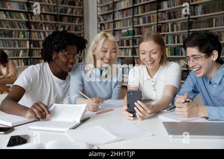 Fröhliche, fröhliche, multiethnische Gruppe von Studenten, die ein Mobiltelefon teilen Stockfoto